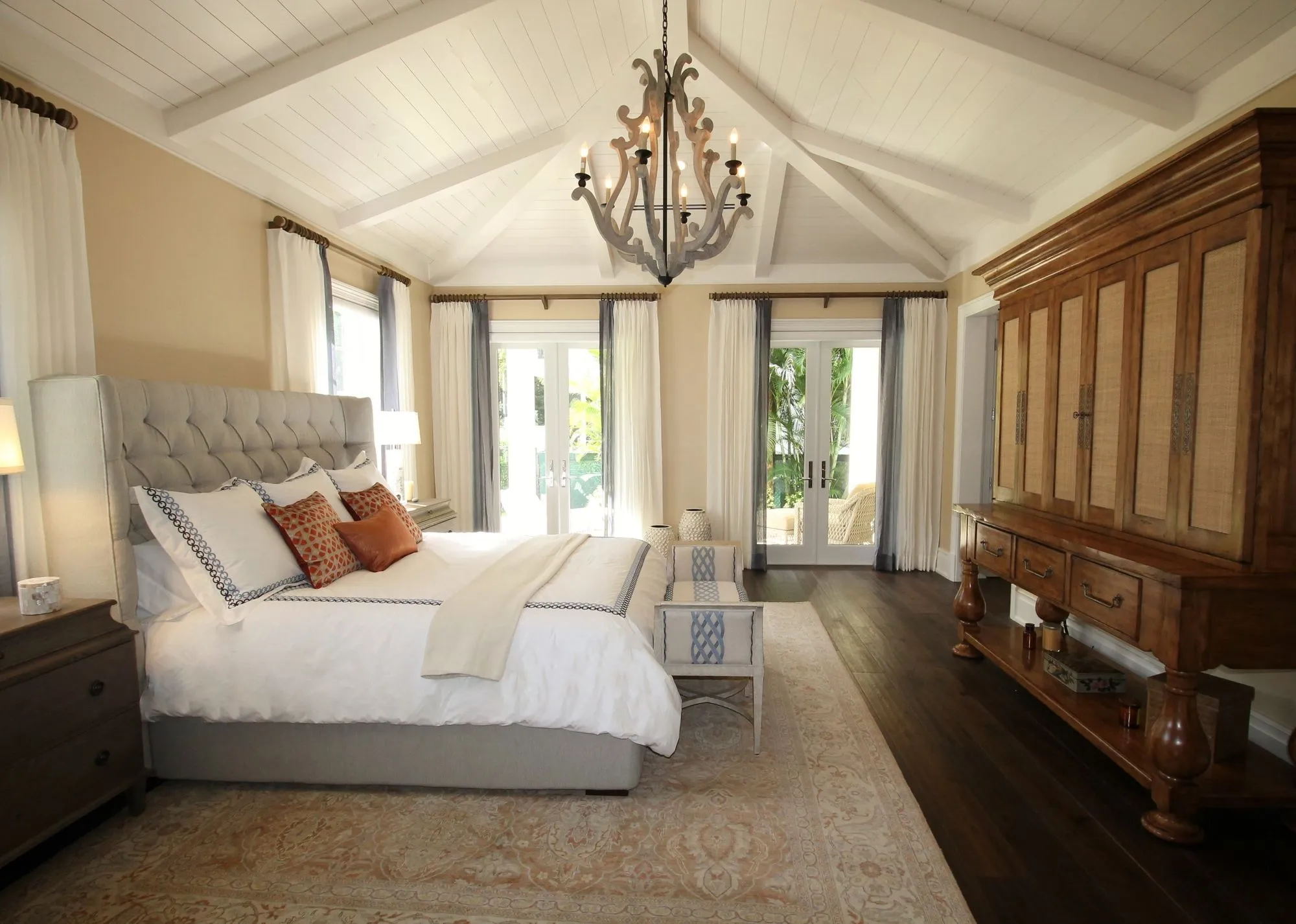 A bedroom with a chandelier, carved wooden cabinet and tall French doors