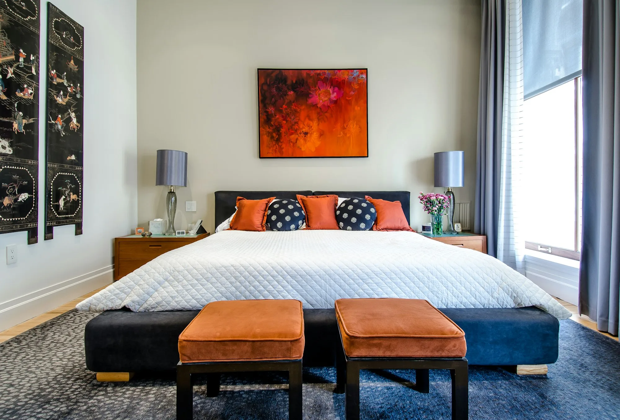 A bedroom with orange stools, a patterned rug and bold cushions
